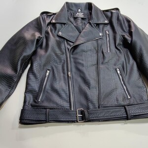 Może przedstawiać: Czarna kurtka motocyklowa ze sztucznej sk&oacute;ry o fakturze sk&oacute;ry węża. Kurtka posiada kołnierz z klapami, asymetryczne zapięcie na zamek błyskawiczny, wiele kieszeni zapinanych na zamek oraz pasek w talii. Pikowana podszewka i srebrne okucia.