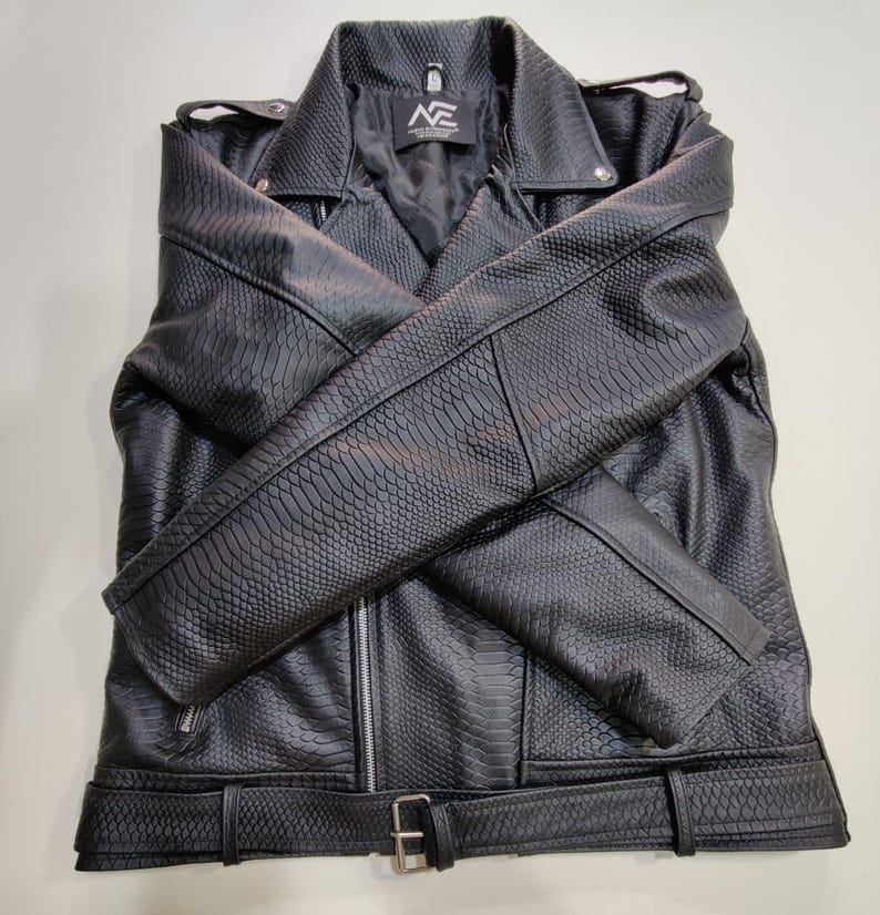 Może przedstawiać: Czarna kurtka ze sztucznej sk&oacute;ry o fakturze sk&oacute;ry węża. Kurtka posiada kołnierz z klapami, zapięcie na zamek błyskawiczny i pasek w talii. Rękawy są złożone z przodu. Kurtka ma litery "NE" na metce.