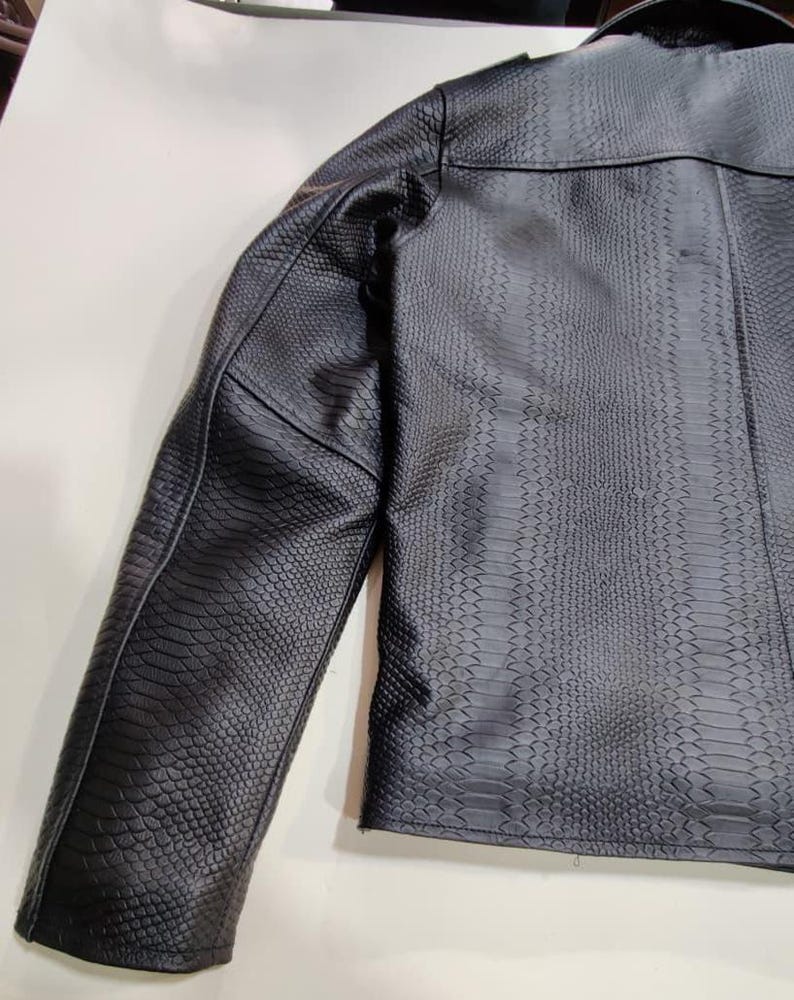 Może przedstawiać: Czarna kurtka ze sztucznej sk&oacute;ry o fakturze sk&oacute;ry węża. Kurtka ma klasyczny kr&oacute;j z wykładanym kołnierzem i dopasowanym krojem. Rękawy są długie, a og&oacute;lny styl jest odważny i nowoczesny.