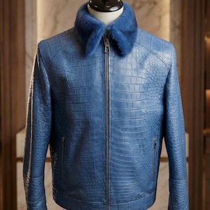 Pode incluir: Casaco de couro azul com textura de pele de crocodilo. O casaco tem gola de pele azul e zíper prateado. O casaco é exibido em um manequim. O casaco tem dois bolsos laterais com zíper.