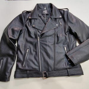 Może przedstawiać: Czarna kurtka motocyklowa ze sztucznej sk&oacute;ry z fakturą sk&oacute;ry węża. Posiada asymetryczne zapięcie na zamek błyskawiczny, kilka kieszeni zapinanych na zamek i pasek w talii. Kurtka ma kołnierz z klapami i srebrne detale.