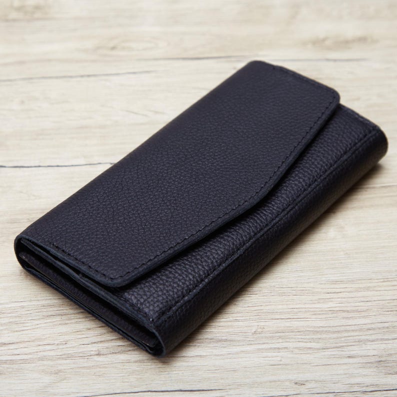 A black leather wallet or purse is placed on a wooden surface.