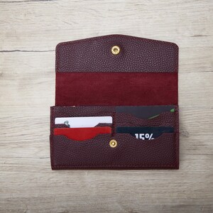 A burgundy leather wallet with a card slot and two cards inside, placed on a wooden surface.