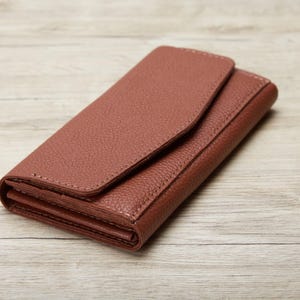 A brown leather wallet or purse is placed on a wooden surface.
