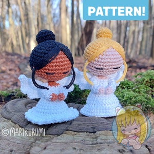 Puede incluir: Dos figuritas de ángel de crochet con vestidos blancos, una con cabello negro y piel marrón y la otra con cabello rubio y piel rosa. Los ángeles están de pie sobre un tocón de árbol con musgo verde.
