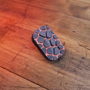 Puede incluir: Una alfombrilla de ratón de goma negra y roja con un patrón geométrico. La alfombrilla de ratón está sobre una superficie de madera.