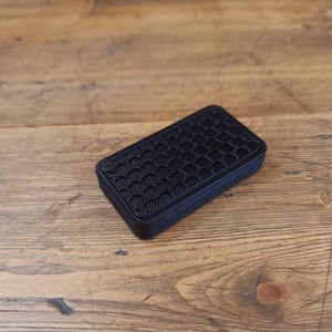 Puede incluir: Una pequeña caja rectangular negra con un patrón de panal en la parte superior.