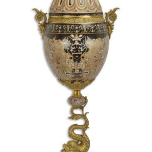 Peut inclure: Urne antique ornée d'un couvercle en dôme et de détails dorés complexes. Le corps noir et or de l'urne présente des motifs floraux et est soutenu par un support doré en forme de dauphin. La base et le couvercle sont de couleur beige clair.