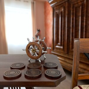 Peut inclure: Six sous-verres en bois brun avec des cercles concentriques sur une table en bois fonc&eacute; avec un volant de bateau en argent et en bois au centre.