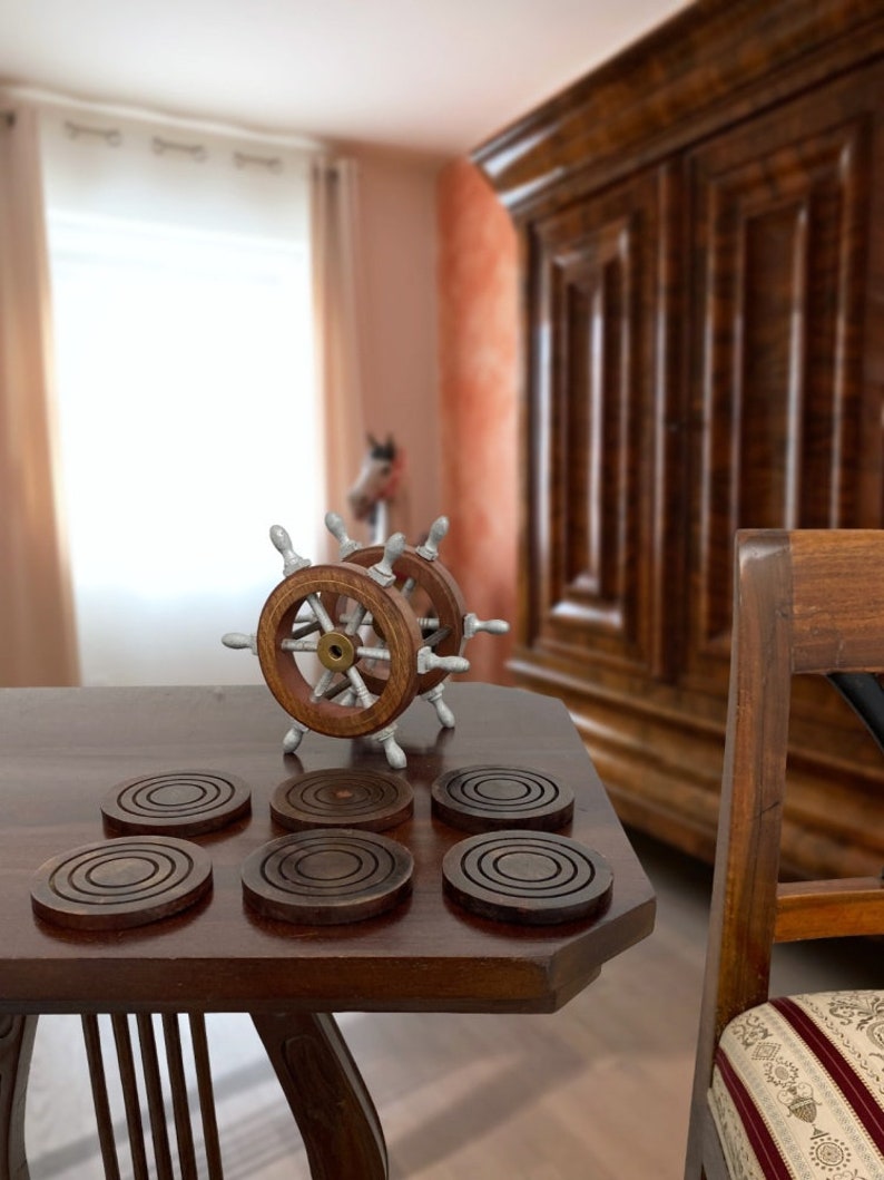 Peut inclure: Six sous-verres en bois brun avec des cercles concentriques sur une table en bois fonc&eacute; avec un volant de bateau en argent et en bois au centre.