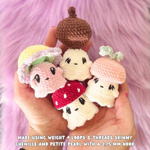 May include: A collection of handmade crochet mushroom and acorn figures in various colors, including pink, red, white, and brown. Each figure has a unique design and facial features. The text at the bottom reads "MADE USING WEIGHT 4 LOOPS & THREADS SKINNY CHENILLE AND PETITE PEARL WITH A 2.75 MM HOOK."