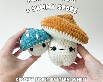 May include: Two crocheted mushroom toys, one teal with white spots and one orange, sit atop a white mushroom. The text "FRANKIE FUNGI + SAMMY SPORE" and "CROCHET FIDGET PATTERN BUNDLE BY CABLE + CANVAS" are displayed.