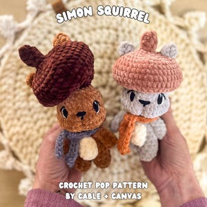Puede incluir: Dos muñecos de ardilla hechos a mano con ganchillo. Uno es marrón con un sombrero de bellota rojo oscuro y una bufanda azul. El otro es gris con un sombrero de bellota rosa y una bufanda naranja. El texto "SIMON SQUIRREL" y "CROCHET POP PATTERN BY CABLE + CANVAS" son visibles.