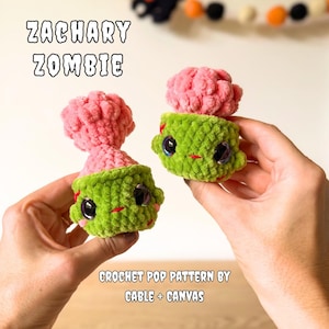 May include: Two small, green, crocheted zombie figures with large, dark, glossy eyes and pink, textured, brain-like tops. The text ZACHARY ZOMBIE and CROCHET POP PATTERN BY CABLE + CANVAS is visible in the image, describing these plush toys.