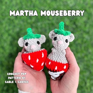 May include: Two crocheted mouse toys, each with a gray body, green leaf-like top, and a red strawberry base with white seeds. The text "MARTHA MOUSEBERRY" is at the top, and "CROCHET POP PATTERN BY CABLE + CANVAS" is at the bottom.