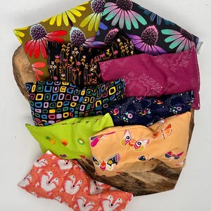 May include: A collection of colorful, patterned fabric pouches. Designs include floral, geometric, and butterfly prints in various colors like pink, green, yellow, and blue. The pouches are arranged on a wooden surface.