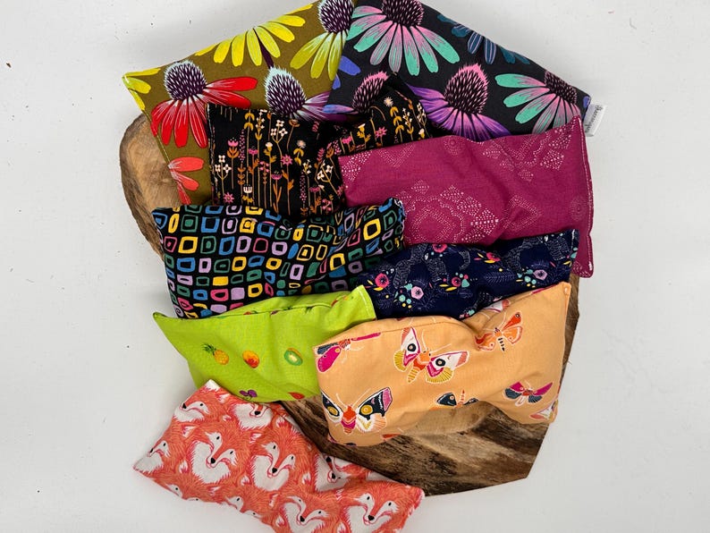 May include: A collection of colorful, patterned fabric pouches. Designs include floral, geometric, and butterfly prints in various colors like pink, green, yellow, and blue. The pouches are arranged on a wooden surface.