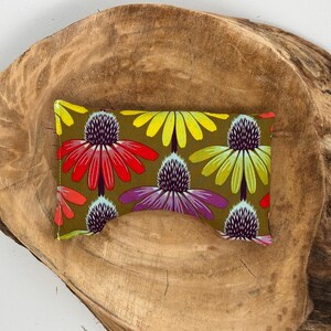 May include: A rectangular fabric item with a floral pattern featuring red, yellow, and purple flowers on an olive green background. The item is placed on a rustic, brown wooden surface.