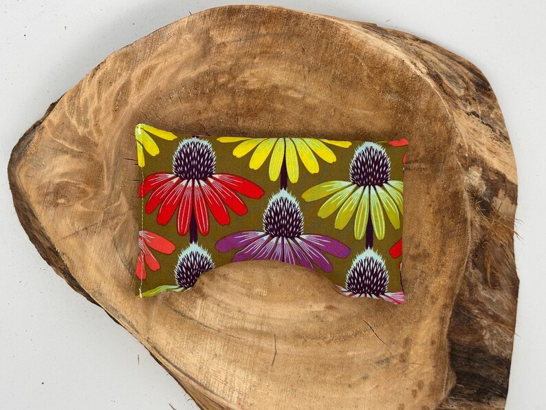 May include: A rectangular fabric item with a floral pattern featuring red, yellow, and purple flowers on an olive green background. The item is placed on a rustic, brown wooden surface.