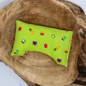 May include: A small, lime green pillow with a fruit pattern, including strawberries, pineapples, grapes, and kiwi. The pillow is rectangular with a curved indentation on one side. The pillow is on a wooden surface.