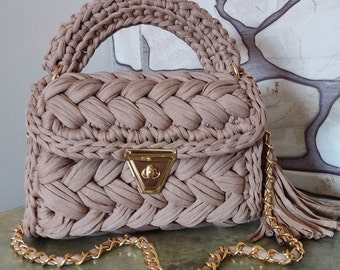 May include: A beige crocheted handbag with a gold chain strap and tassel. The bag has a braided design and a gold clasp.