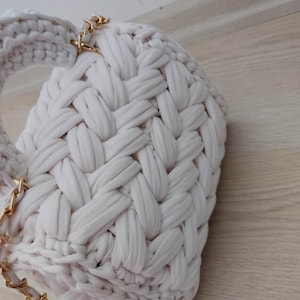 May include: A white crocheted bag with a gold chain strap and fringe detail.