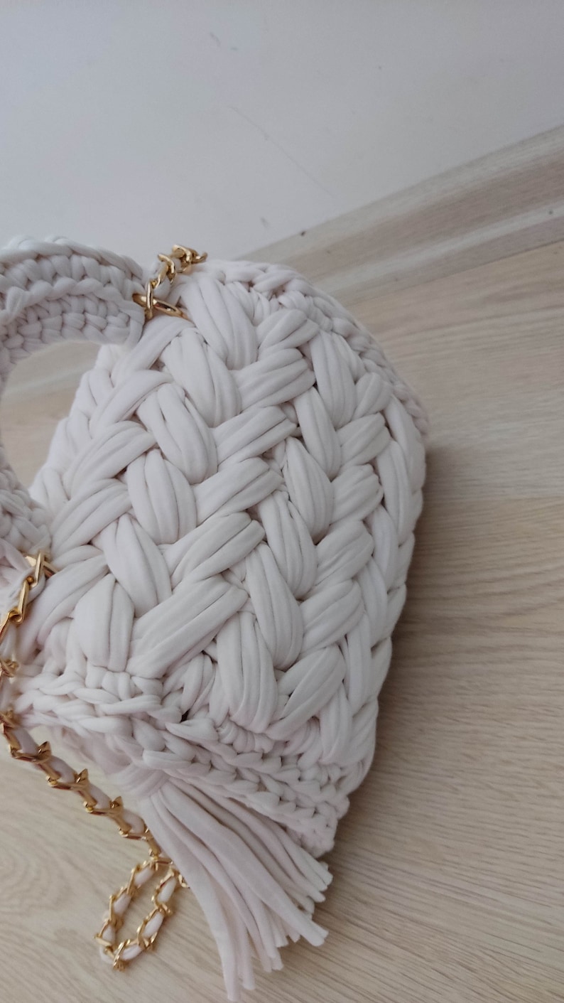 May include: A white crocheted bag with a gold chain strap and fringe detail.