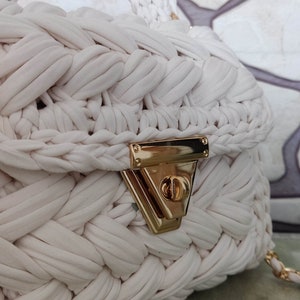 May include: White crocheted handbag with a gold clasp and a gold chain strap.