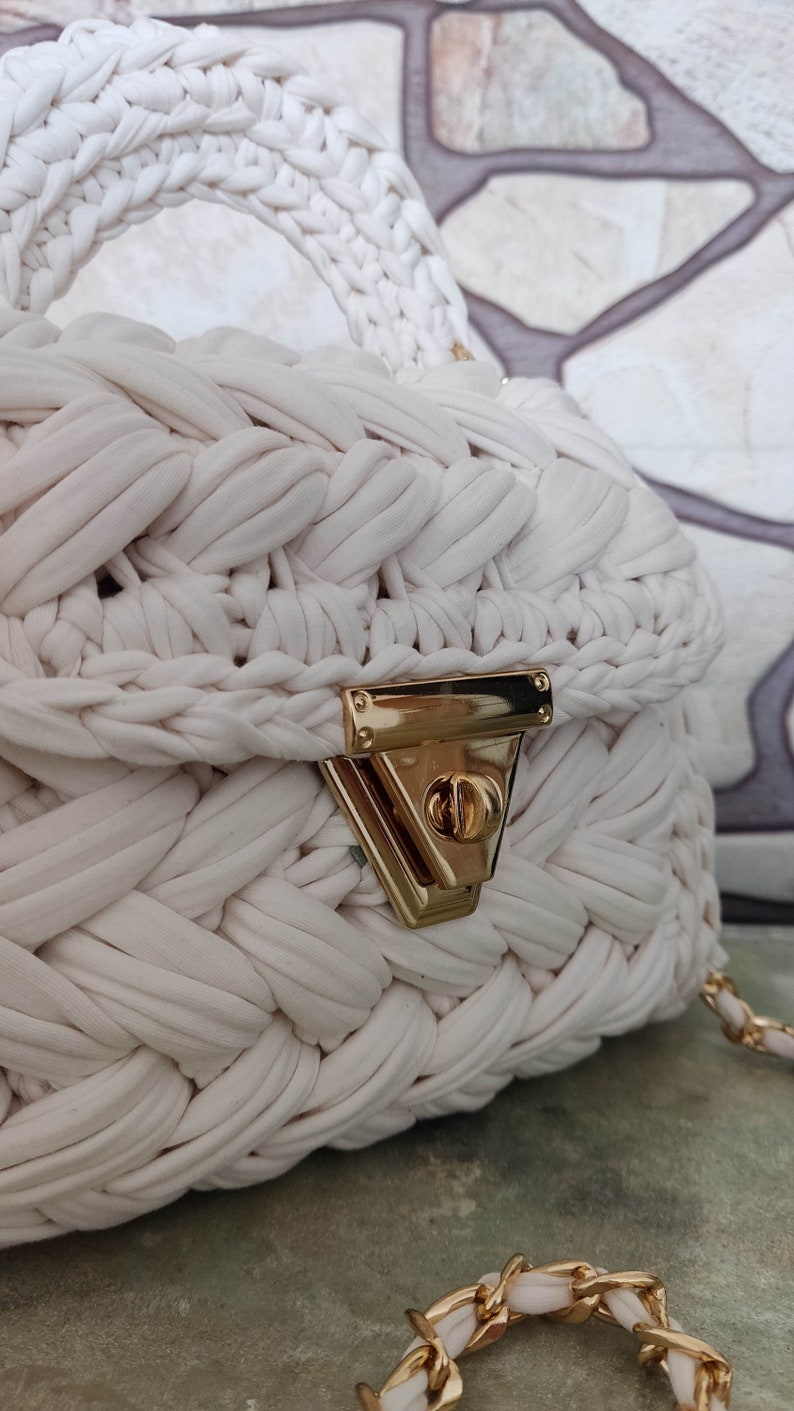 May include: White crocheted handbag with a gold clasp and a gold chain strap.
