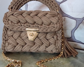 May include: A brown crocheted handbag with a gold chain strap and a gold clasp. The bag has a braided design and a tassel.