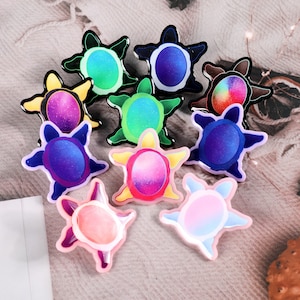 May include: Assortment of colourful turtle-shaped pins with different designs. Each pin features a different colour and pattern, including purple, blue, green, pink, and yellow.