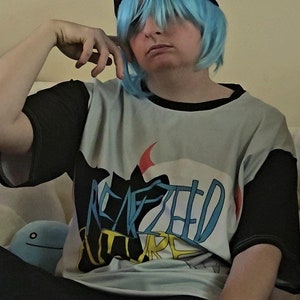 May include: A person wearing a black and red beanie with a blue wig, a black and white graphic t-shirt with the text "REPEATED FUTURE" and black pants.