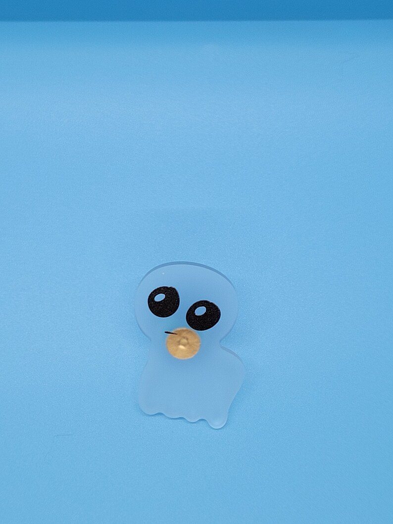 May include: A translucent blue ghost with black eyes and a gold coin in its mouth. The ghost is on a light blue background.