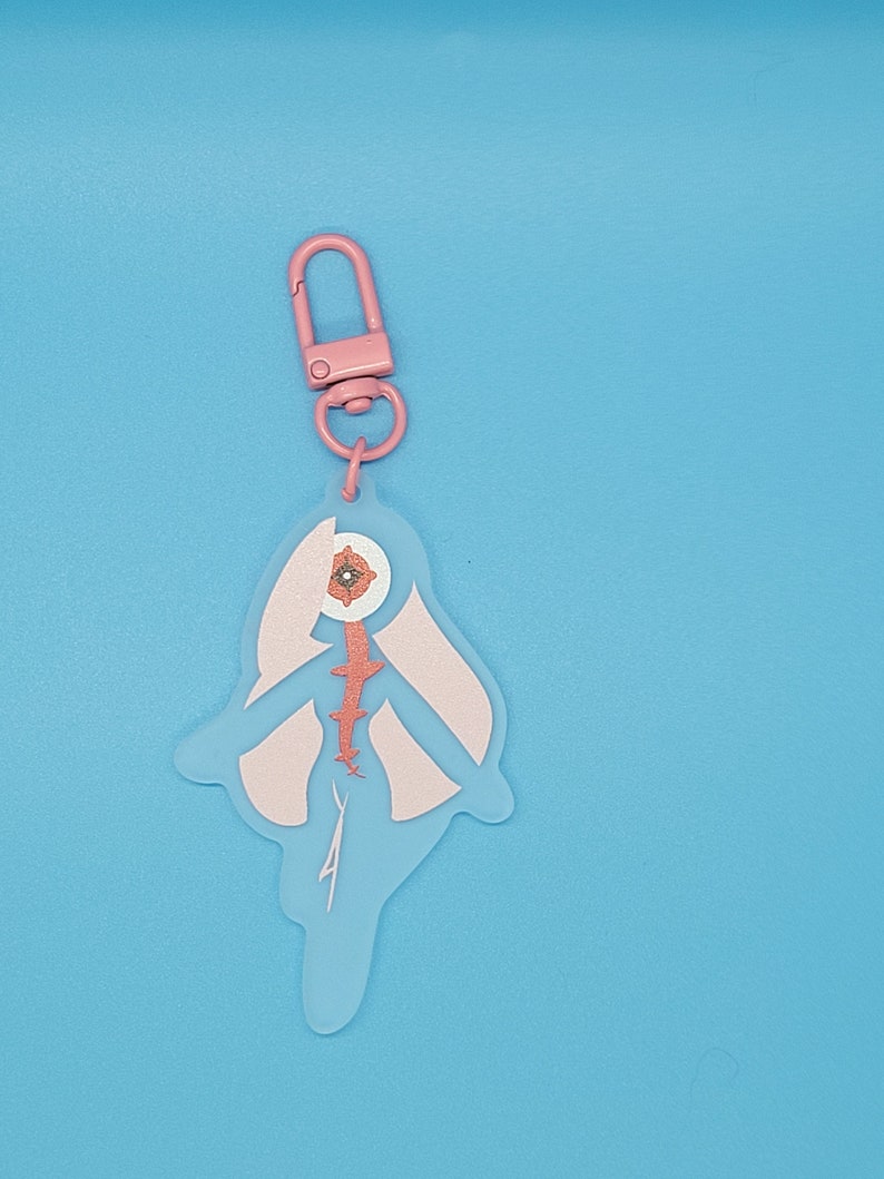Puede incluir: Llavero rosa con una figura transl&uacute;cida de una persona con un ojo grande y una flor rosa en su interior. La figura tiene un dise&ntilde;o rosa y blanco y una columna vertebral roja.
