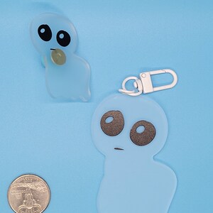 May include: Two blue ghost-shaped keychains with black eyes and a white keychain ring. The larger ghost keychain has a white loop for attaching to a bag or belt.