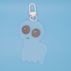 May include: A light blue ghost keychain with a white metal ring. The ghost has two black eyes and a small mouth.