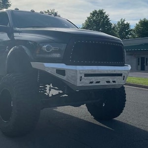 May include: A black pickup truck with a custom front bumper and large tyres. The truck has a blacked-out grille and a silver front bumper.