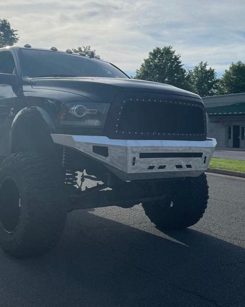 May include: A black pickup truck with a custom front bumper and large tyres. The truck has a blacked-out grille and a silver front bumper.