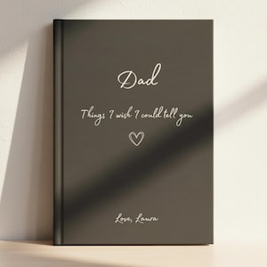 May include: A dark grey hardcover journal with white text that reads Dad, Things I wish I could tell you, and Love, Laura, featuring a small hand-drawn heart icon centred between the text lines on the front cover of the book.
