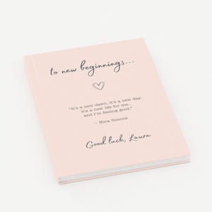 May include: A light pink hardback journal featuring the black text "to new beginnings..." above a small heart icon. Below this, the quote "It's a new dawn, it's a new day. it's a new life for me... and I'm feeling good." - Nina Simone, and "Good luck, Laura."