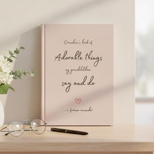 Op de afbeelding: Een lichtroze hardcover boek met de tekst Grandma's book of Adorable things my grandchildren say and do ...a forever reminder en een klein harticoontje gedrukt op de voorkant in een donker handschriftachtig lettertype.