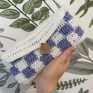 May include: A crocheted clutch bag with a white and purple checkered pattern and a wooden button closure.