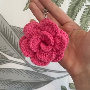 May include: A pink crocheted flower keychain. The flower is made of yarn and has a loop for attaching to a key ring.
