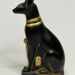 May include: Black and gold Egyptian cat statue with hieroglyphics on the base. The cat is sitting with its head turned to the side.