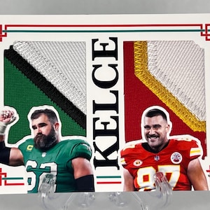 Puede incluir: Una tarjeta coleccionable deportiva con dos jugadores de fútbol americano, uno en verde y otro en rojo. La tarjeta tiene un borde blanco con detalles en rojo y verde y el nombre "KELCE" en negro.