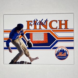 May include: A baseball card featuring a player in a blue and orange uniform, with the name "Finch" in orange script. The Mets logo is in the lower right corner. The card has a white background with blue and orange stripes.