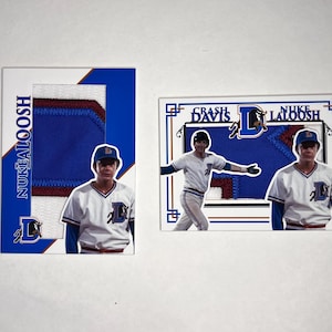 Könnte beinhalten: Zwei Baseballkarten mit Spielern der Baseballteams Crash Davis und Nuke LaLoosh. Die Karten sind weiß mit blauen und roten Akzenten. Die Karten zeigen Fotos der Spieler in ihren Uniformen.