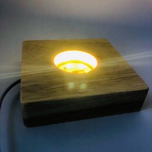 May include: A wooden base with a circular cutout in the centre. The cutout is illuminated with a warm yellow light.