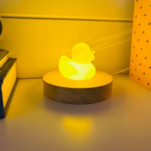 May include: A yellow rubber duck night light on a wooden base. The duck is lit up and glowing.