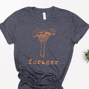 May include: A dark heather grey t-shirt with an orange illustration of a mushroom and the word "forager" printed in orange.